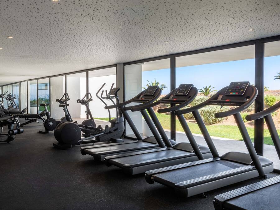 Un gimnasio con cintas de correr, bicicletas estáticas y pesas.