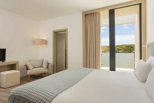 Habitación de hotel con cama, una silla, escritorio, televisor y balcón con cortinas.