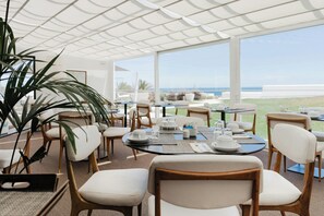 A dining area with tables set for service, chairs, and a large potted plant. - Memmo Baleeira - Design Hotels (Vila do Bispo)