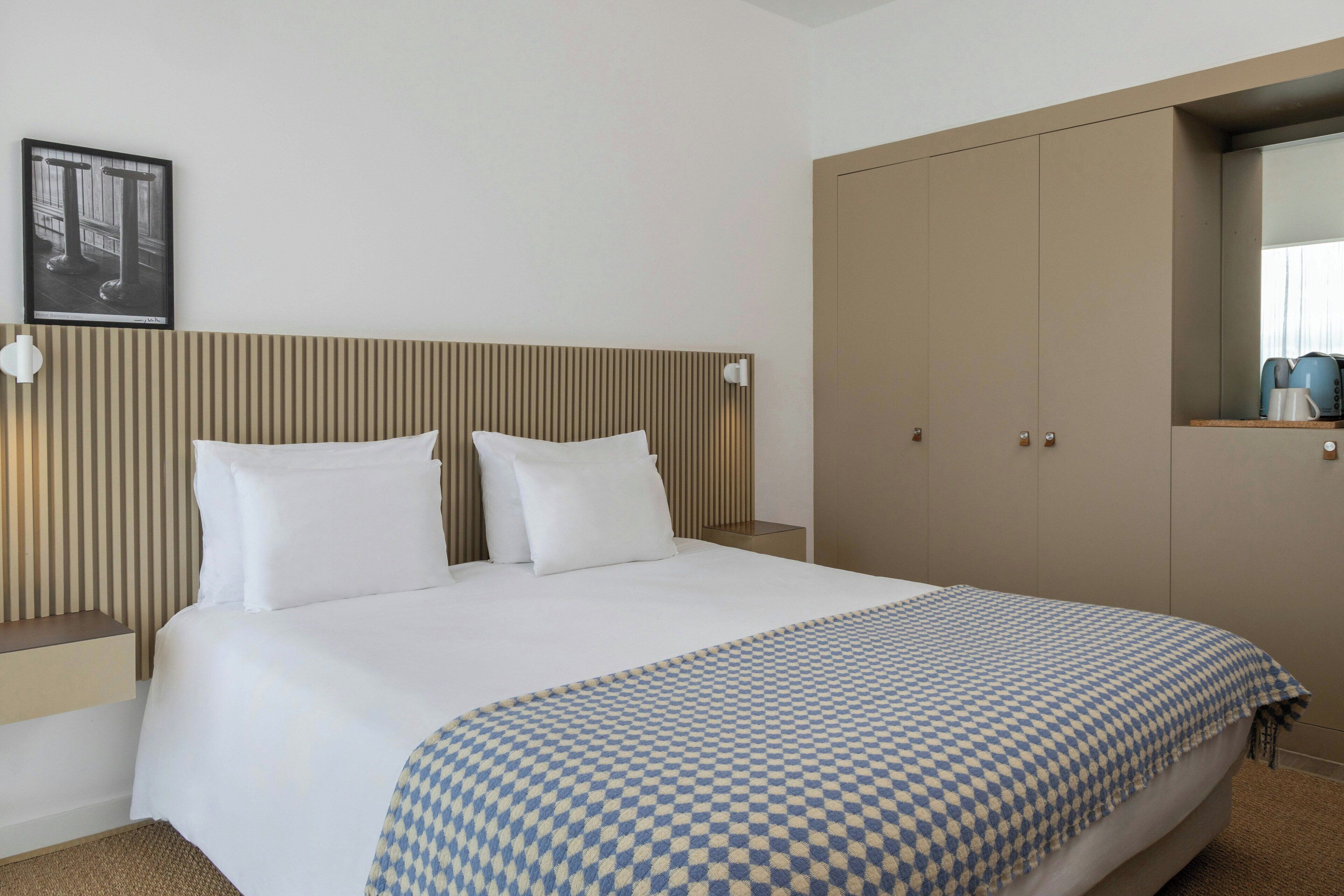 Ein Hotelzimmer mit einem großen Bett, einem Holzkopfteil, einem Kleiderschrank und einem gerahmten Bild an der Wand.