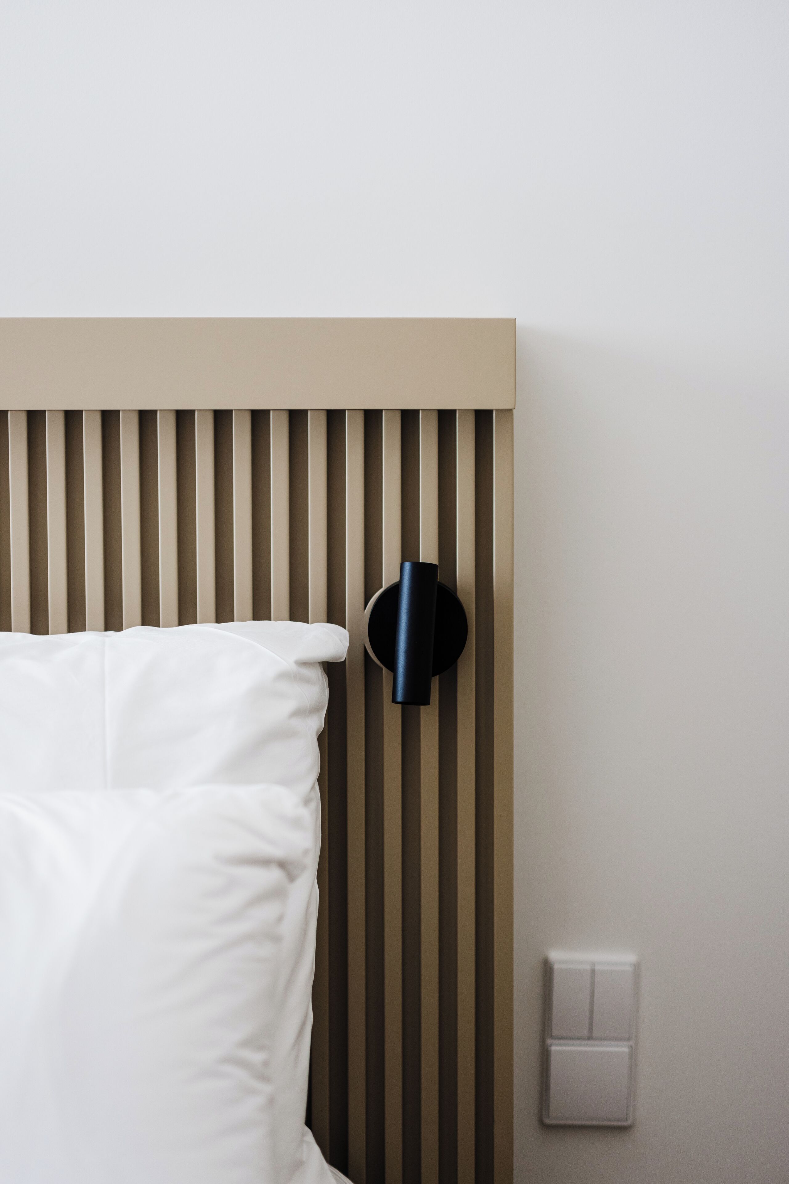 A bed with white bedding, a wall-mounted light fixture, and a light switch.