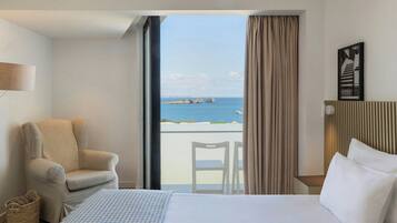 Habitación de hotel con cama, una silla, una mesita, una lámpara y vistas al mar.