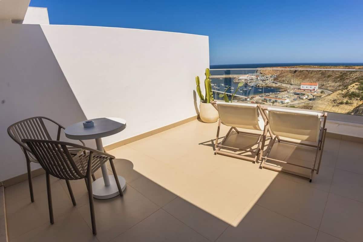 A balcony with a table and chairs, a potted plant, and a view of the coastline.