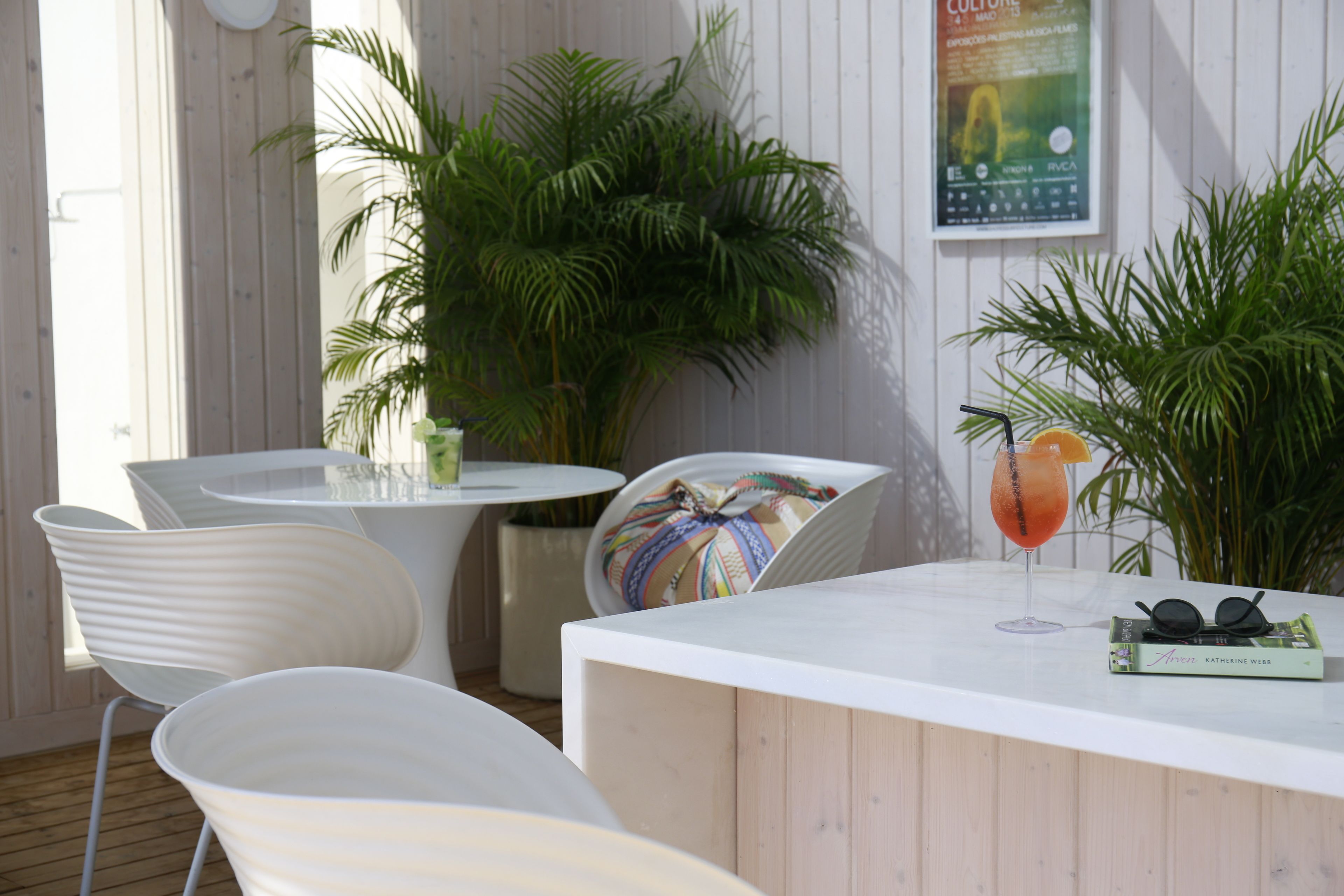 A modern outdoor seating area with white chairs and a white table, surrounded by lush green plants.