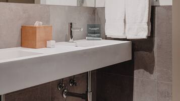 Un baño moderno con un espejo grande, un lavamanos blanco, un banco de madera y un perchero para toallas.
