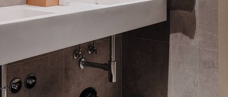 A modern bathroom with a large mirror, a white sink, a wooden bench, and a towel rack.