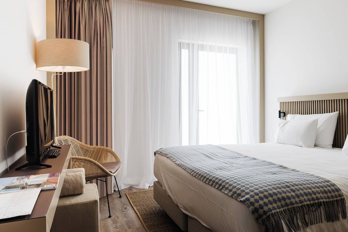 A hotel room with a bed, a desk with a computer, a chair, and a lamp.