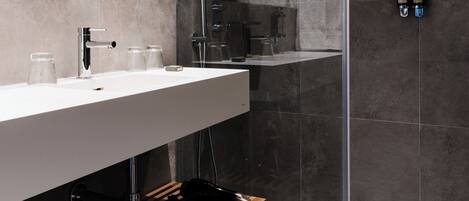 Un baño moderno con cabina de ducha de vidrio, un lavamanos blanco y dos botellas de champú en la pared.