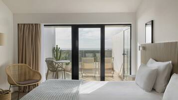 A hotel room with a bed, a chair, a table, and a view of the outdoors.