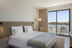 A hotel room with a large bed, a chair, a table, and a balcony with a view. - Memmo Baleeira - Design Hotels (Vila do Bispo)