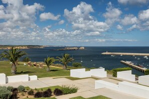 A coastal hotel with white structures, a marina with boats, and a clear sky. - Memmo Baleeira - Design Hotels (Vila do Bispo)