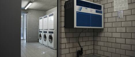 A laundry room with a large industrial dryer and a wall-mounted air conditioning unit.