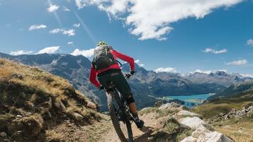 Ciclista de montanha numa trilha com vista para montanhas e um lago.