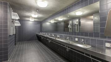 A public restroom with dark tiled walls, a long counter with multiple sinks, and overhead lighting.