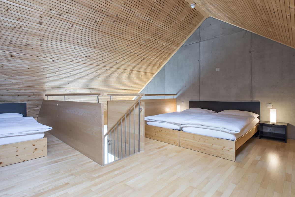 A bedroom with a sloped ceiling, wooden flooring, and a bed with white bedding.