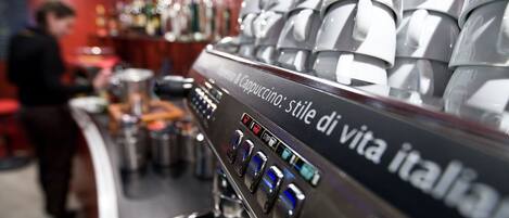 Une machine à café avec plusieurs tasses empilées au-dessus, et une personne qui travaille derrière le comptoir.