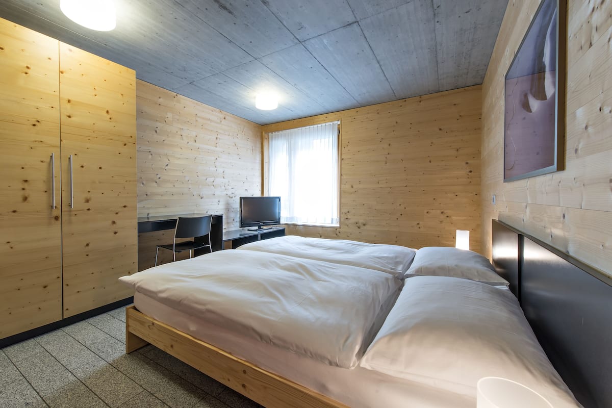 A bedroom with a bed, wooden wardrobe, desk, and a television.