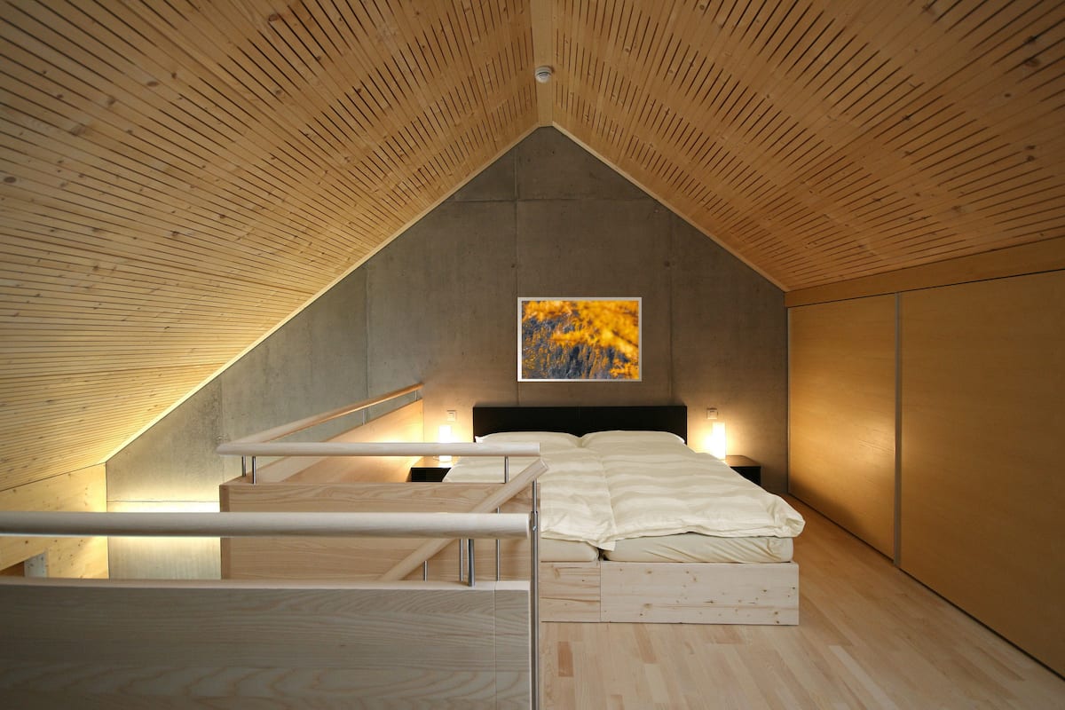 A bedroom with a sloped ceiling, a bed with white bedding, a nightstand, and a painting on the wall.