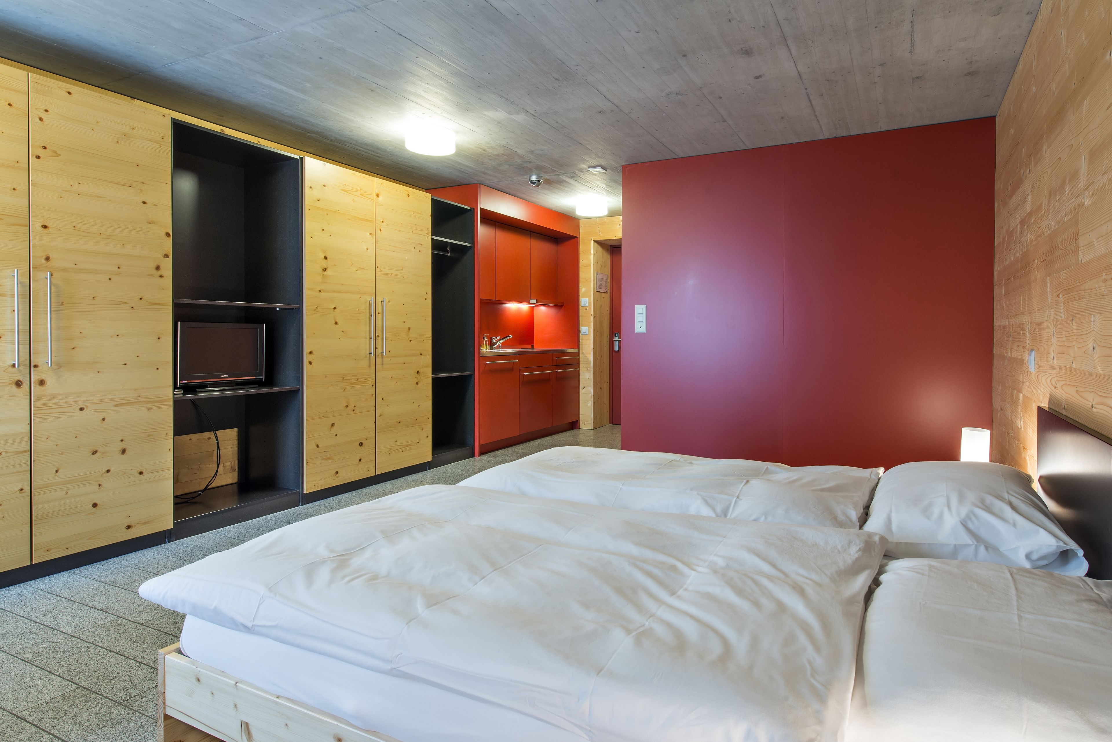 Une chambre à coucher avec un lit, une armoire en bois et un mur rouge.