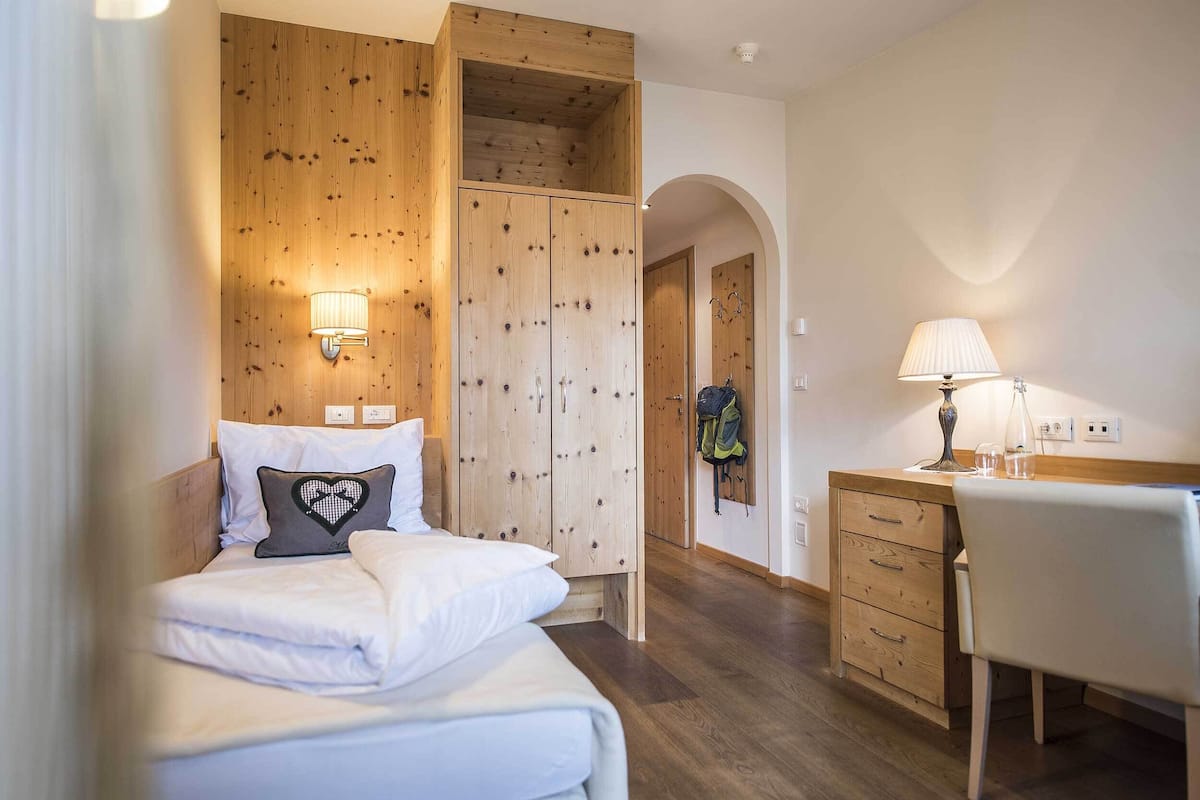 Une chambre avec une armoire en bois, un lit avec une literie blanche, un bureau avec une chaise et une lampe.