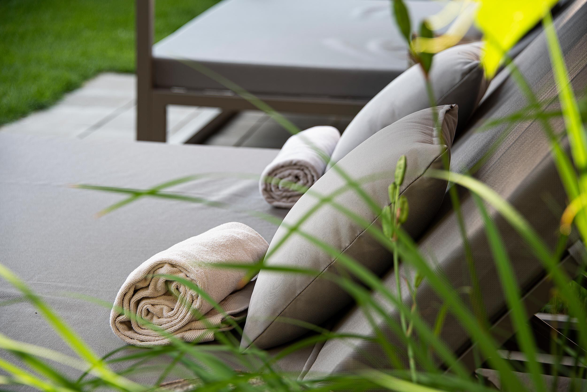 A sun lounger with rolled towels and cushions, surrounded by greenery.