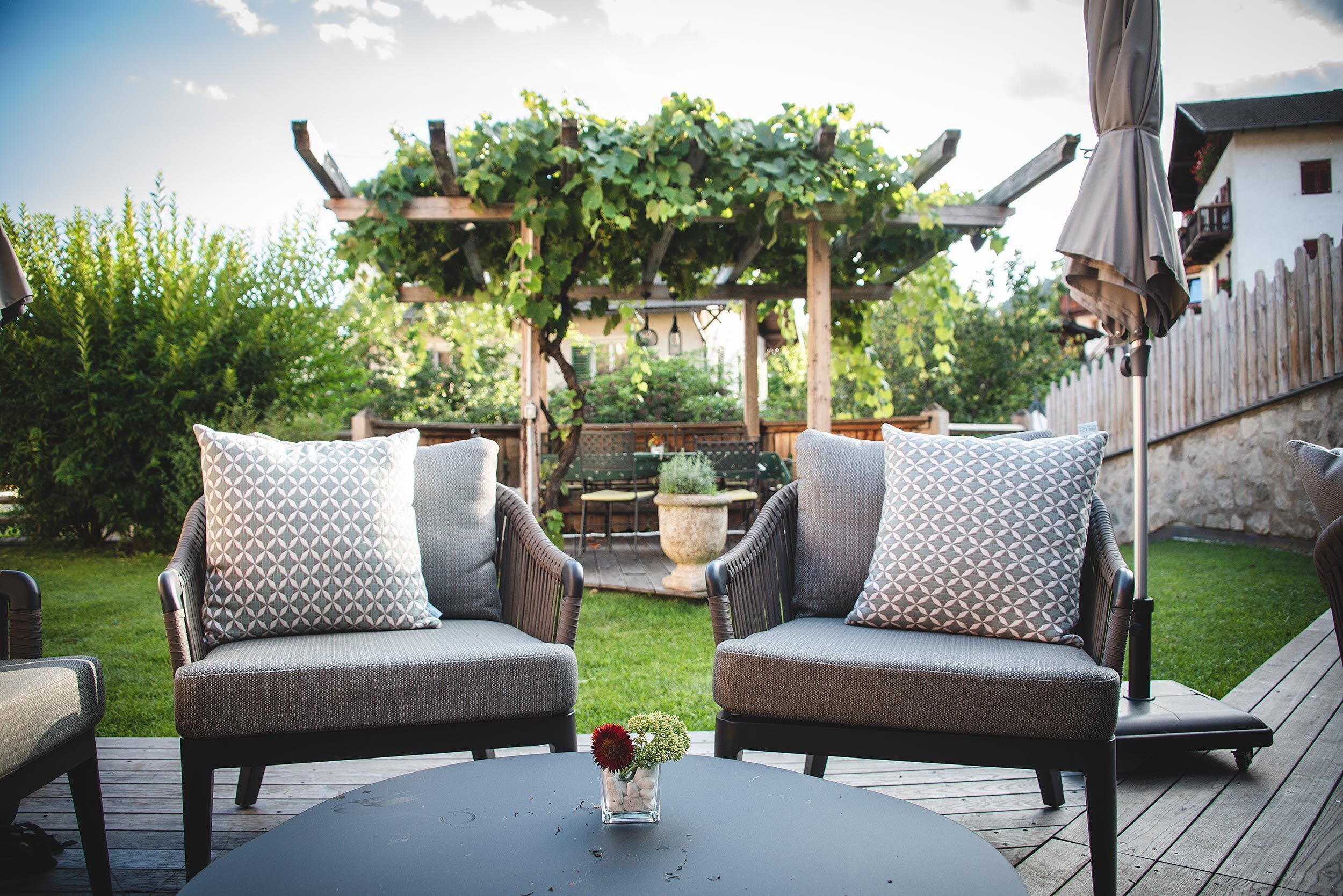 An outdoor patio with two wicker chairs, a round table, and a small vase with flowers.