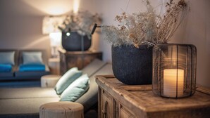 A cozy living room with a sofa, cushions, a wooden side table, a potted plant, and a candle in a glass holder.