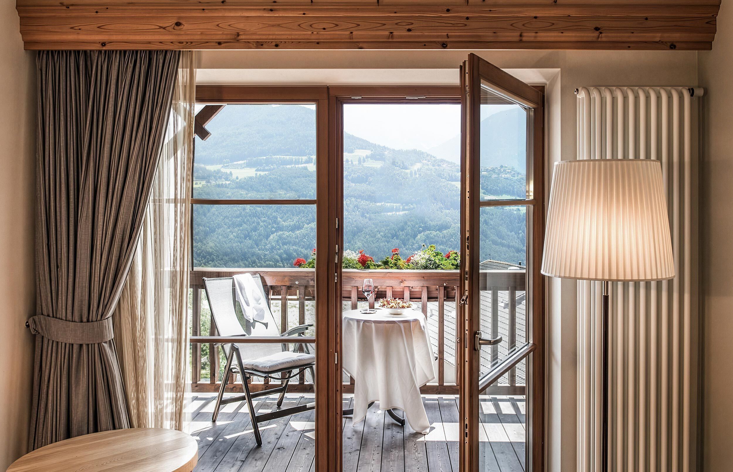 Une pièce avec un plafond en bois, une vue sur un paysage montagneux par de grandes fenêtres, une table à manger avec une chaise et une lampe.