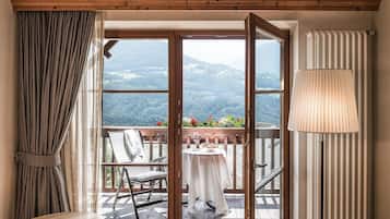 A room with a wooden ceiling, a view of a mountainous landscape through large windows, a dining table with a chair, and a lamp.