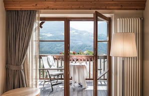 A room with a wooden ceiling, a view of a mountainous landscape through large windows, a dining table with a chair, and a lamp.