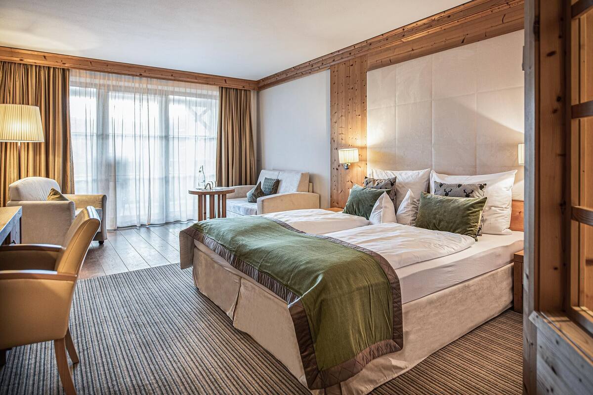 Une chambre d’hôtel avec un grand lit, un coin salon avec une table et des chaises, et une fenêtre avec des rideaux.