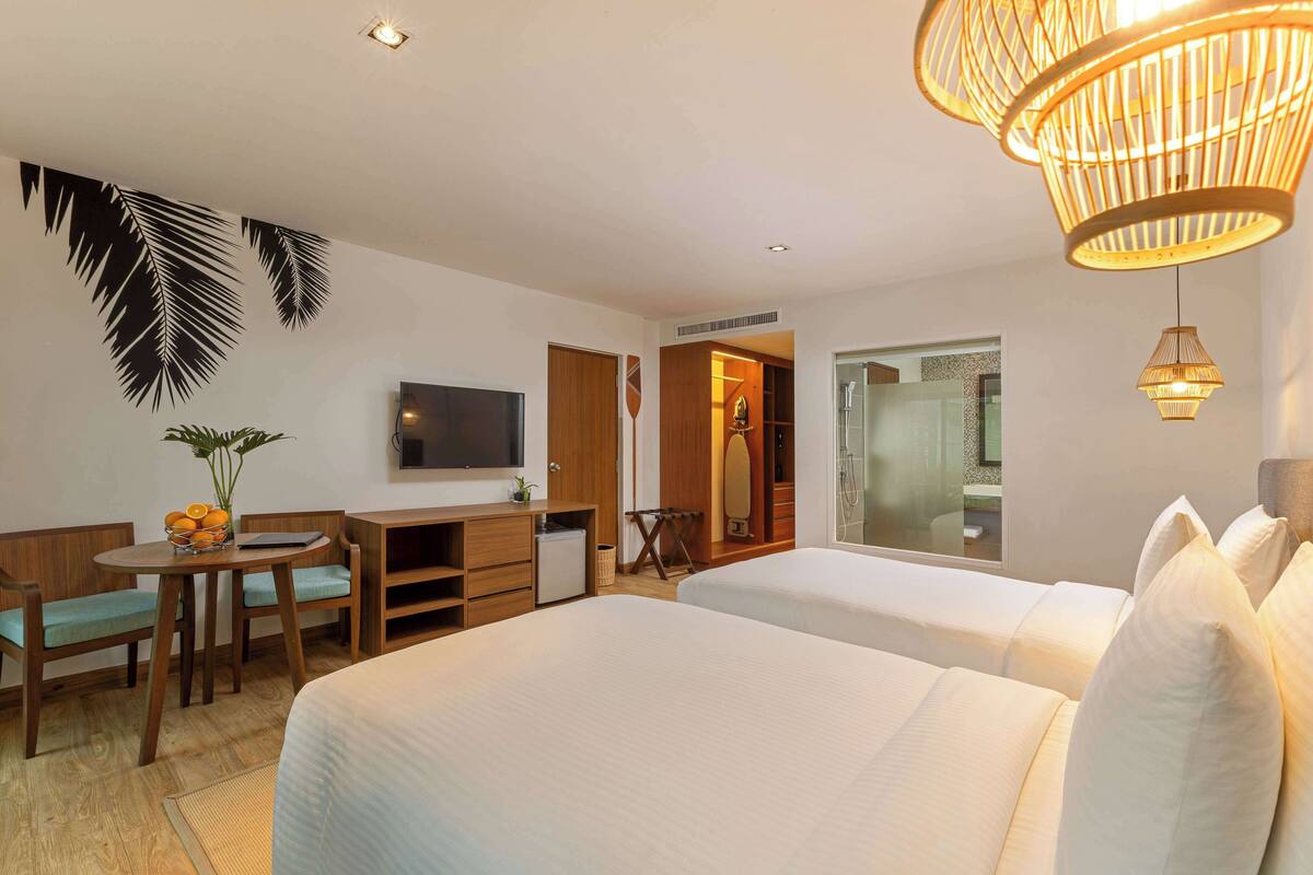 Une chambre d’hôtel avec deux lits, un bureau avec des chaises, une télévision et une grande fenêtre.
