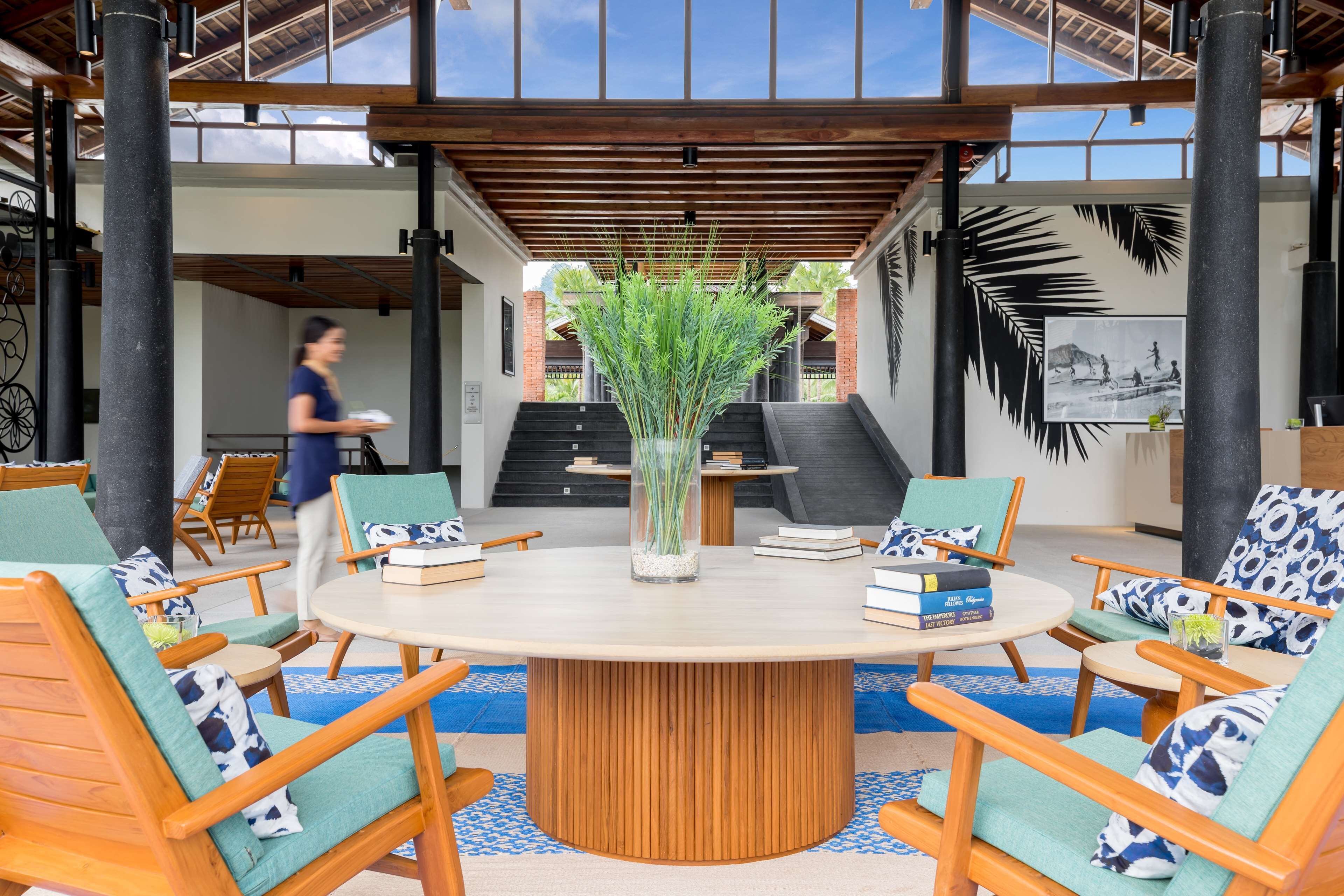 Un espacio interior moderno con una mesa redonda de madera rodeada de sillas, un jarrón decorativo y libros.