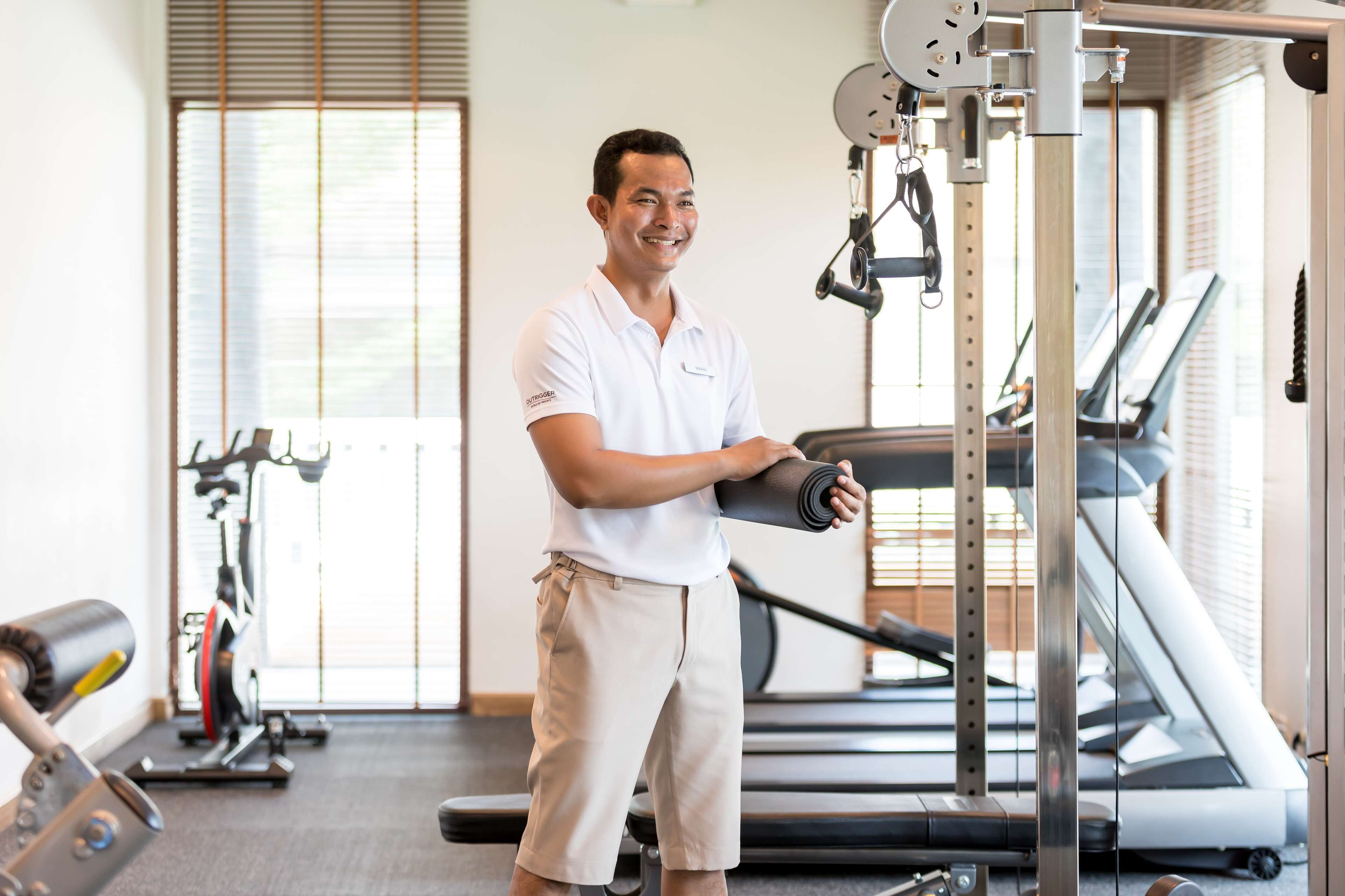 A gym with exercise equipment, a treadmill, and a person holding a yoga mat.