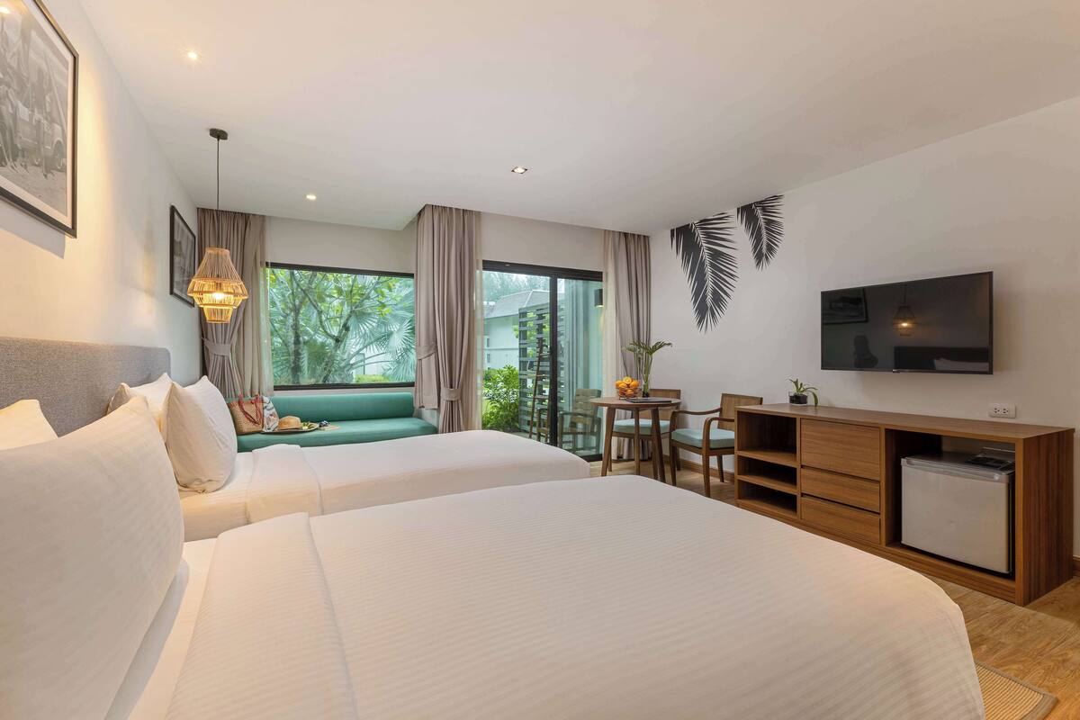 Une chambre d’hôtel avec deux lits, un bureau avec une chaise, une télévision et un balcon donnant sur un espace verdoyant.