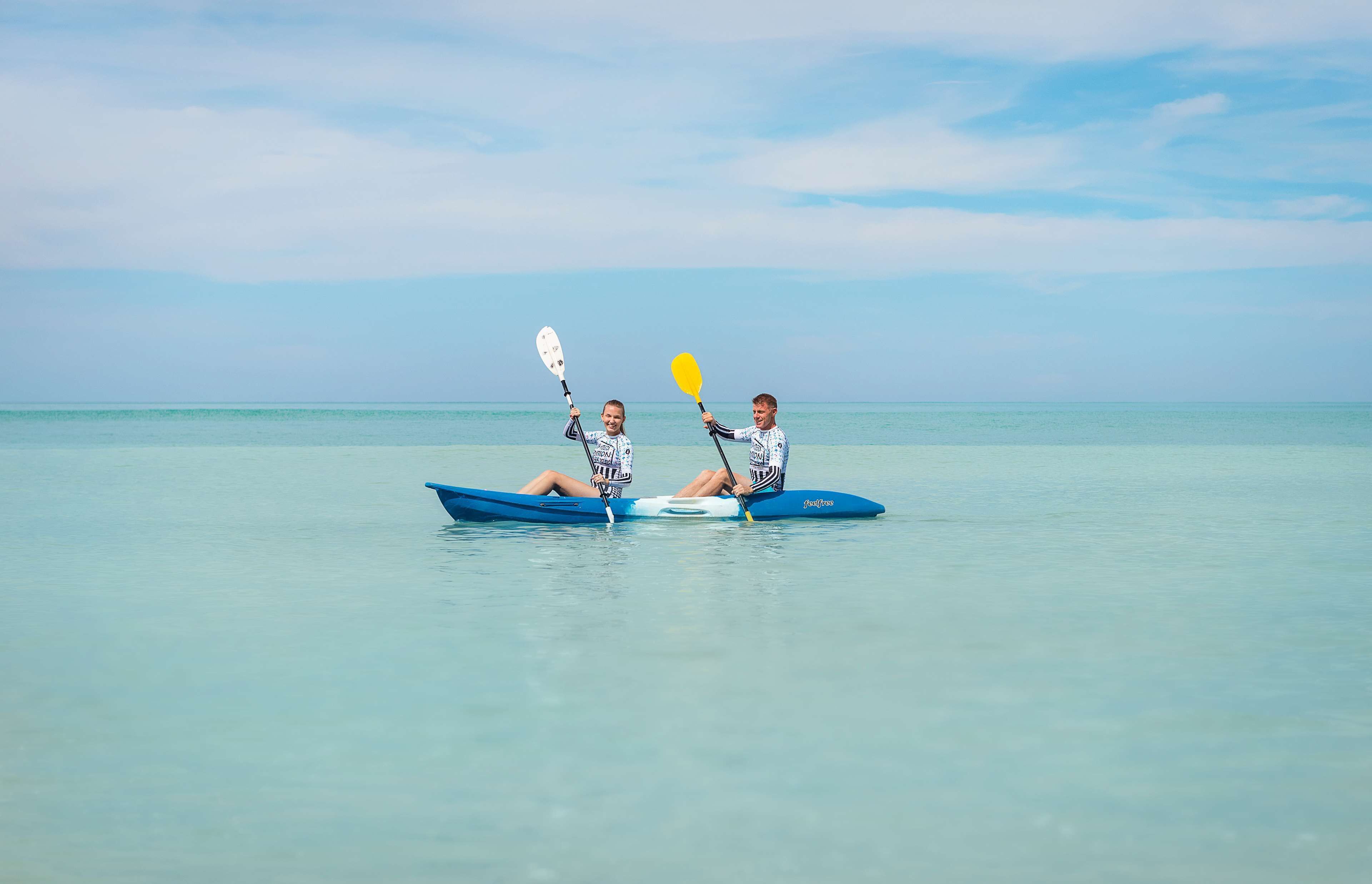 Two people kayaking on a calm sea with a clear sky.