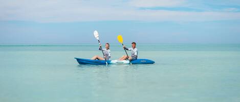 Two people kayaking on a calm sea with a clear sky.