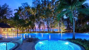 A swimming pool with a tiled edge, surrounded by palm trees and a building with outdoor seating.