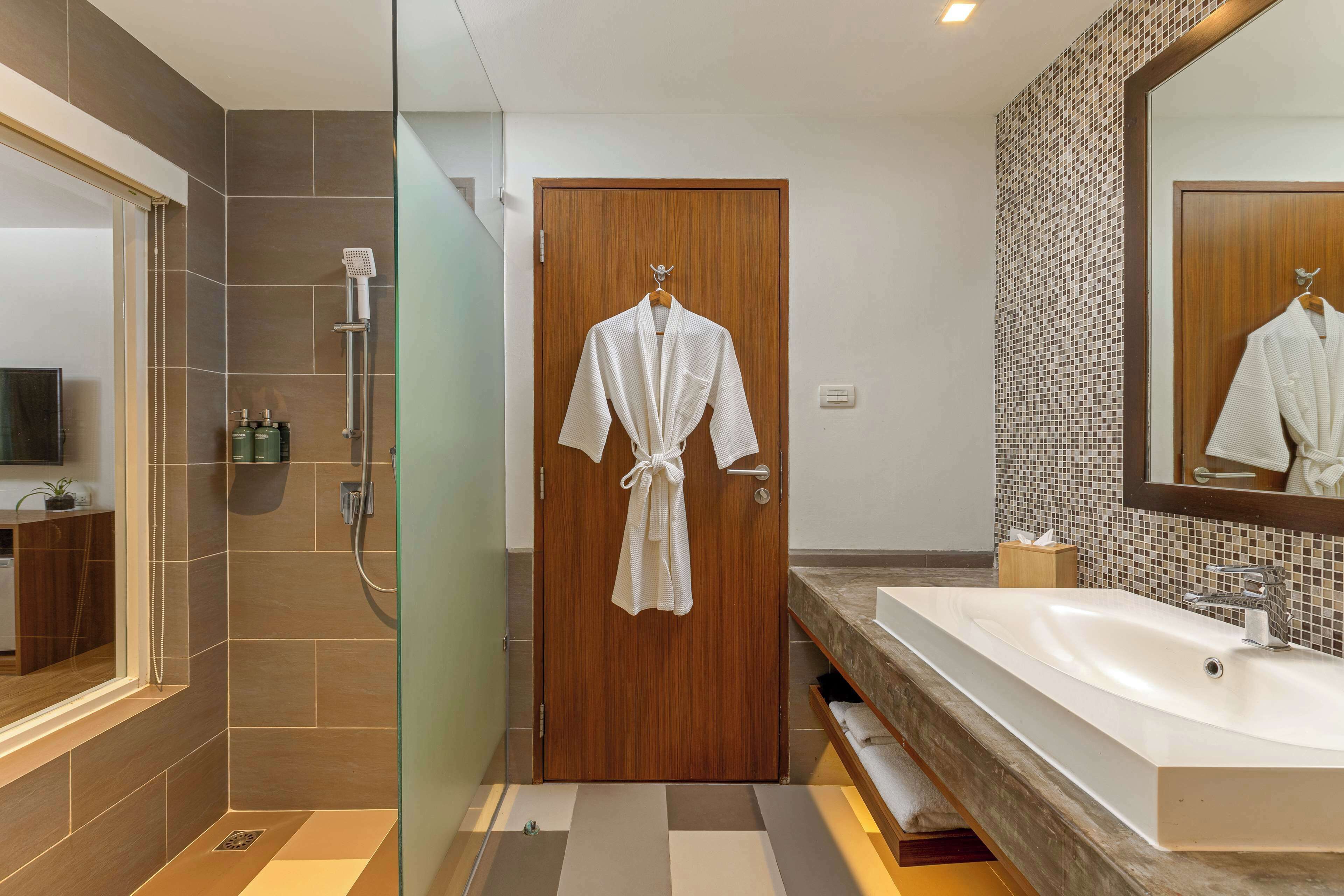 A modern bathroom with a wooden door, a large mirror, a white sink, and a shower area.