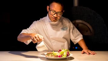 A chef in a white uniform pouring sauce onto a plate of food.