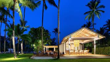 Un resort con zona de estar exterior techada, palmeras y un interior bien iluminado.