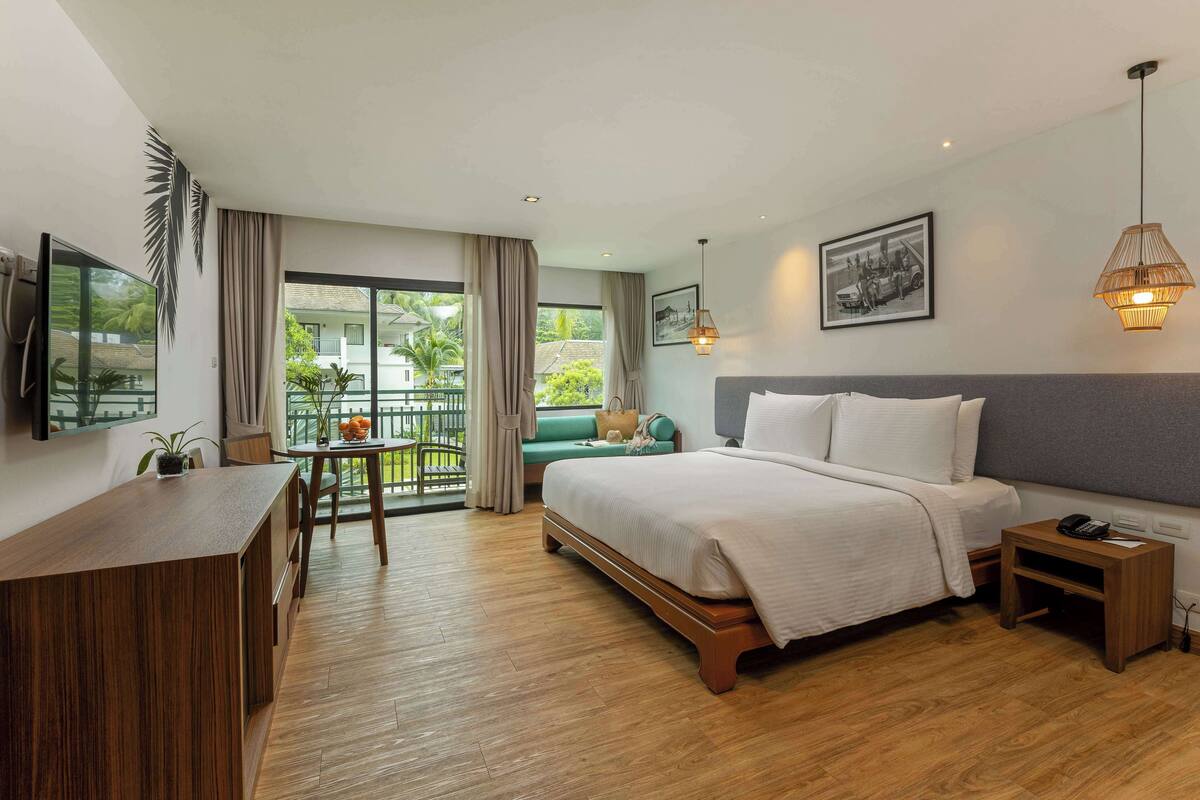 Une chambre d’hôtel comprenant un lit, un bureau, une chaise, une petite table, un balcon avec vue et un luminaire suspendu.