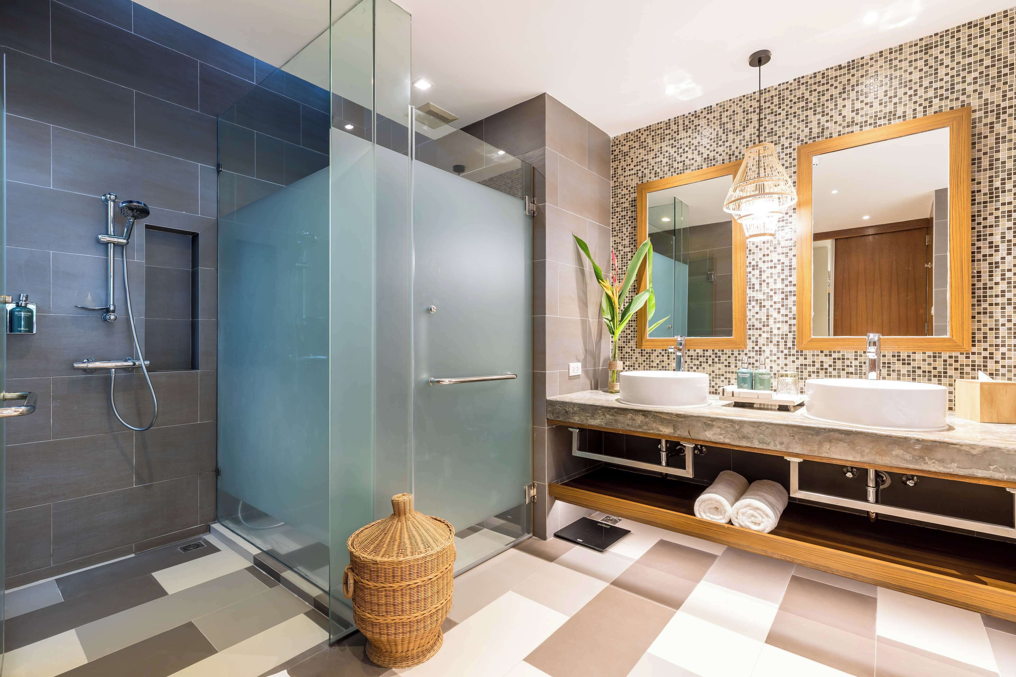 Une salle de bain moderne dotée d’une douche à parois de verre, d’un meuble-lavabo avec deux vasques et d’un miroir décoratif.