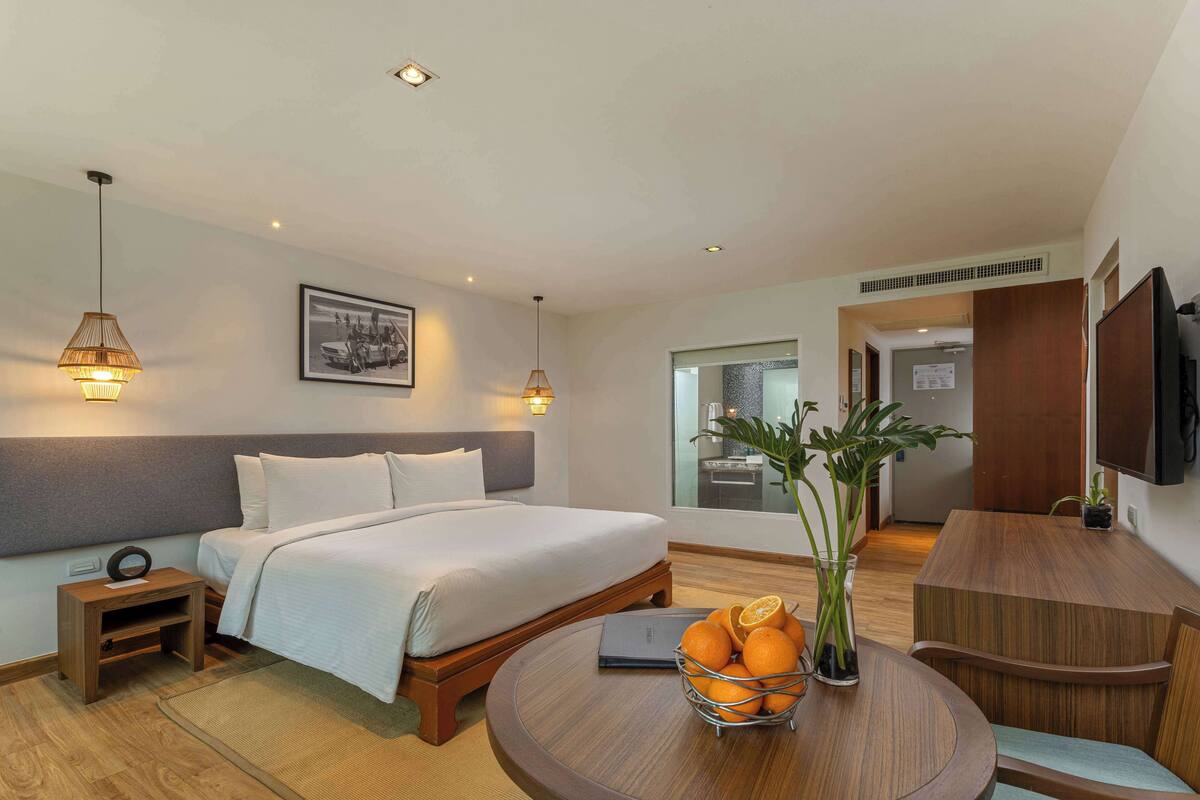 Une chambre d’hôtel avec un lit, une table de chevet, une lampe et une table ronde ornée d’un vase de fleurs.