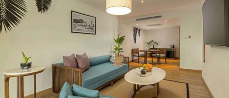 A modern living room with a sofa, coffee table, and chairs, a dining area with a table and chairs, and a kitchen in the background.