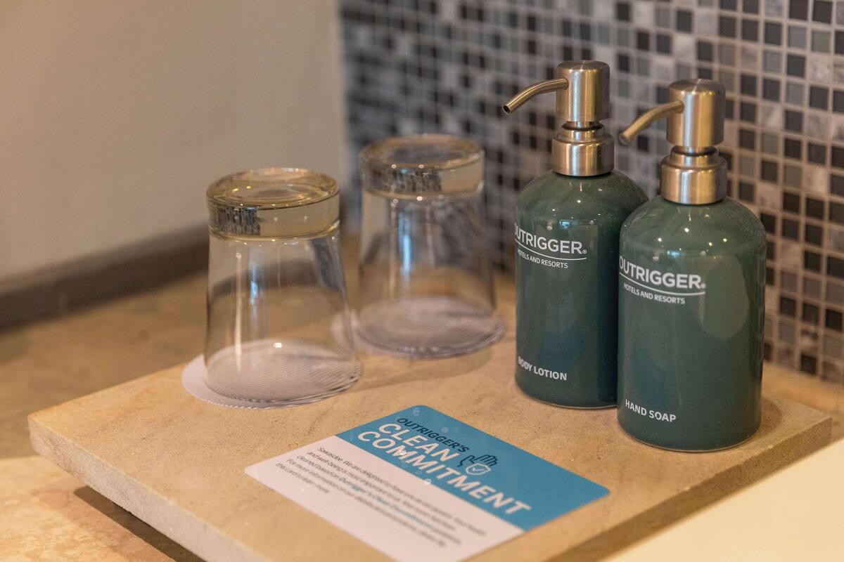 Un meuble-lavabo de salle de bain avec deux flacons de savon liquide, un récipient en verre et un panneau indiquant l’engagement en faveur de la propreté.