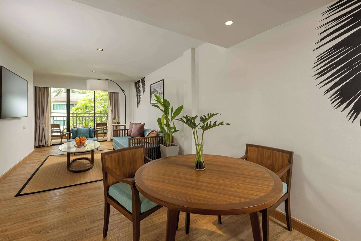 Un salon moderne avec une table ronde en bois, deux chaises, un canapé, un téléviseur et une grande fenêtre avec des rideaux.