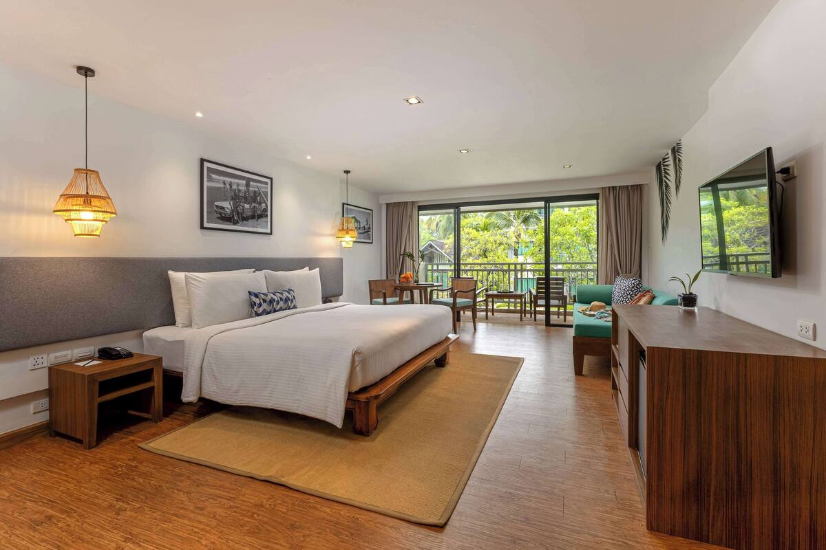 Une chambre d’hôtel moderne, dotée d’un grand lit, d’une table de chevet, d’une lampe et offrant une vue sur l’extérieur grâce à un balcon.