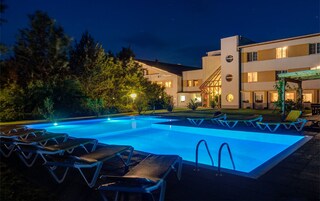 Una piscina con sillas de descanso, un edificio bien iluminado con varias ventanas y un jardín.