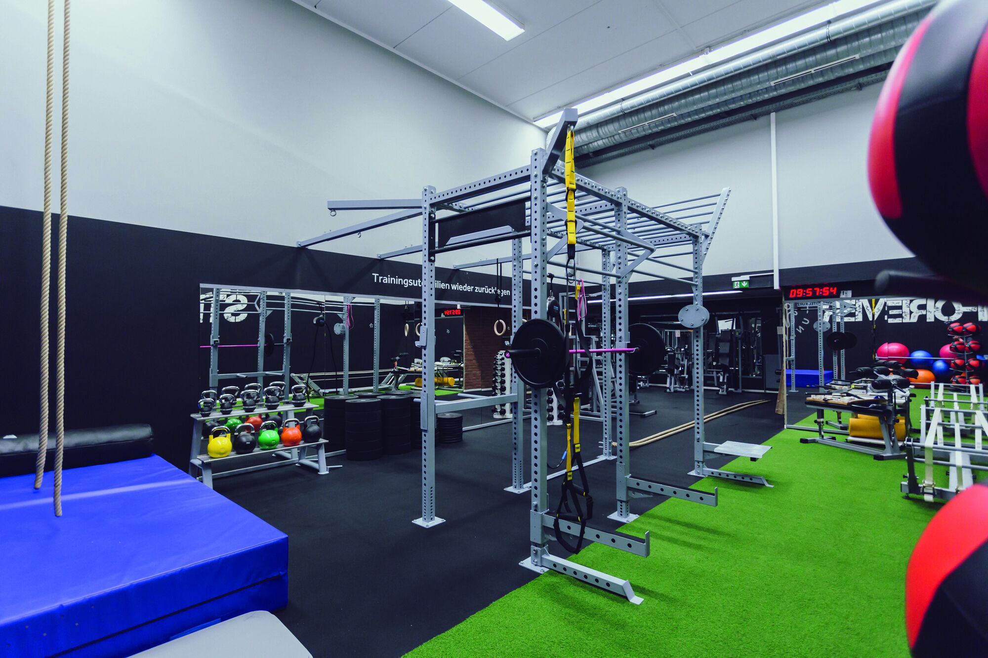 A gym with weightlifting equipment, a blue mat, and a green turf area.